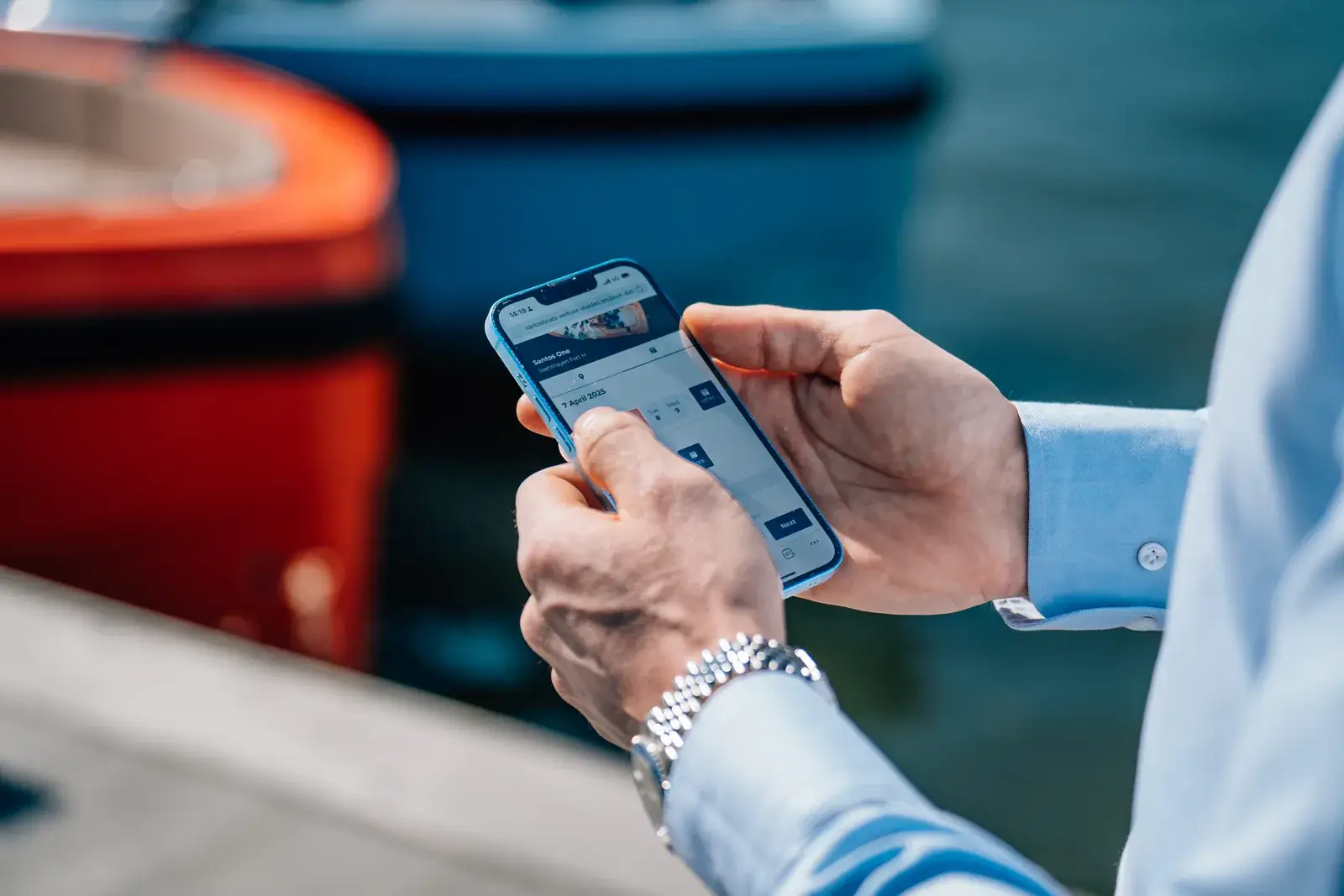 Handen met een telefoon waarop een boeking openstaat, aan de rand van een steiger