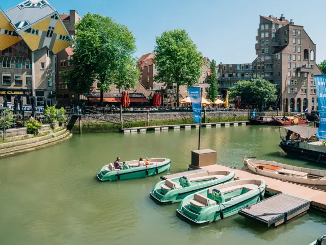 Groene huurboten aan een steiger in de Oude Haven van Rotterdam, met de kubuswoningen erachter
