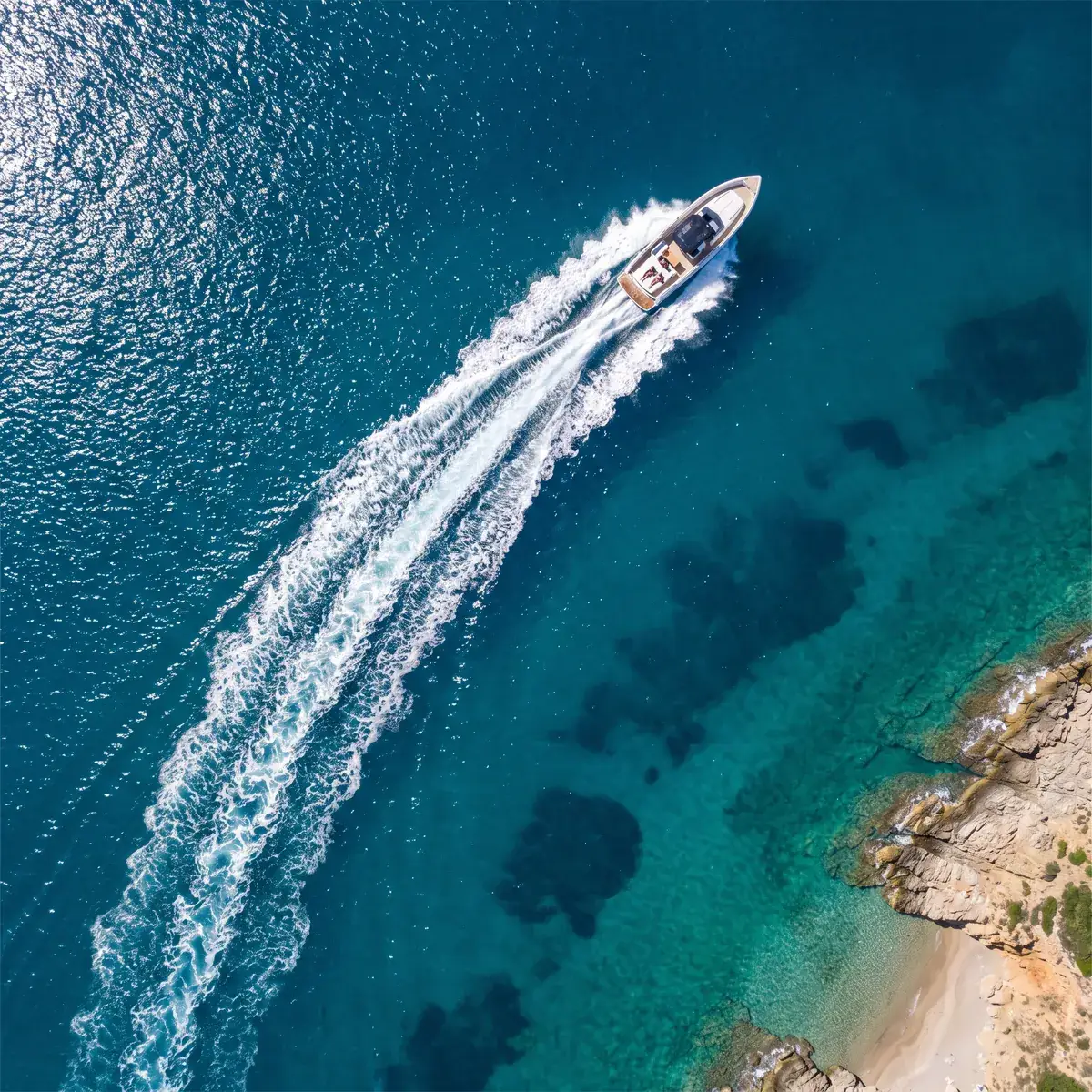 Eén open boot steekt een turquoise baai over en trekt een lange witte lijn door het water, van bovenaf
